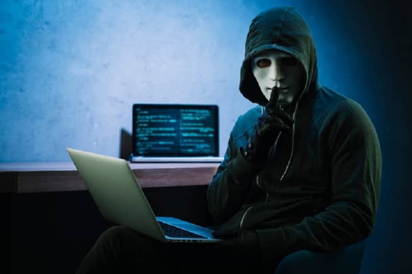 una persona con una máscara blanca y una computadora portátil en la mano